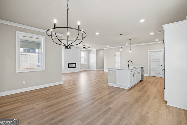 kitchen with pendant lighting, a fireplace, an island with sink, sink, and white cabinets