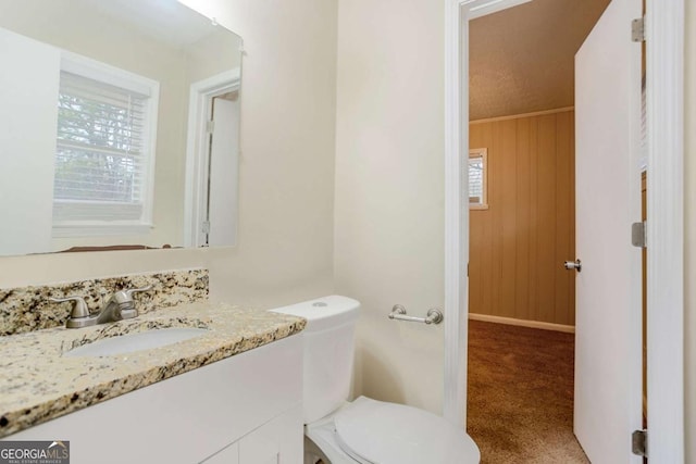 bathroom with toilet, plenty of natural light, wooden walls, and vanity