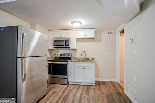 kitchen featuring sink, white cabinetry, light wood-type flooring, stainless steel appliances, and light stone countertops