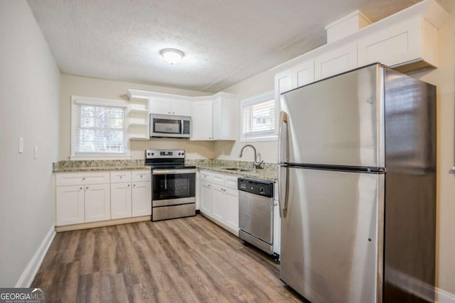 kitchen with sink, appliances with stainless steel finishes, white cabinetry, light stone countertops, and light hardwood / wood-style floors