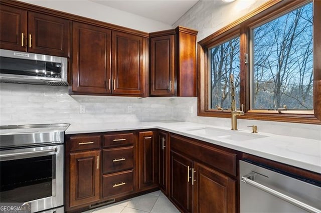 kitchen featuring light tile patterned flooring, sink, decorative backsplash, stainless steel appliances, and light stone countertops