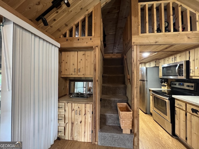 kitchen featuring vaulted ceiling, appliances with stainless steel finishes, wooden walls, light brown cabinets, and light hardwood / wood-style flooring