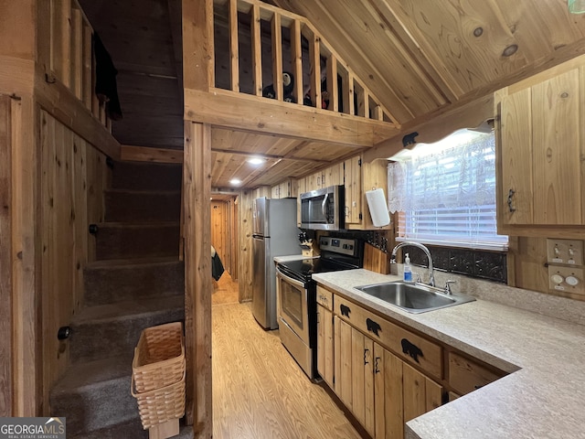 kitchen with wooden walls, lofted ceiling, sink, stainless steel appliances, and light wood-type flooring