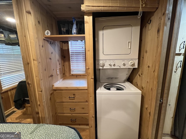 washroom with stacked washer / drying machine and wood walls