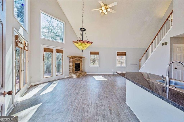 unfurnished living room with french doors, sink, high vaulted ceiling, dark hardwood / wood-style flooring, and a fireplace