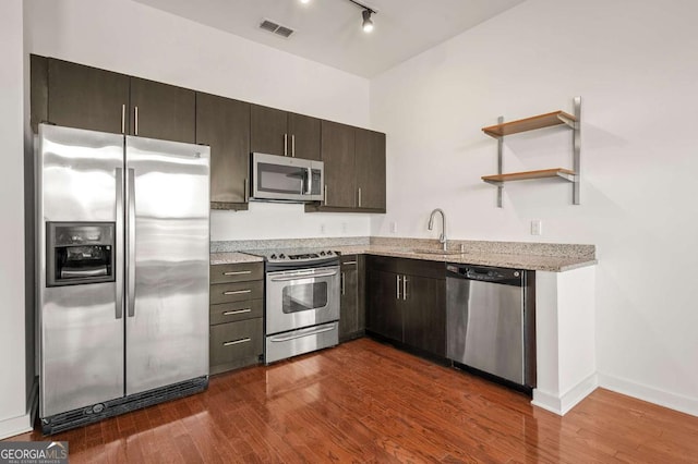 kitchen with sink, rail lighting, appliances with stainless steel finishes, dark brown cabinets, and dark hardwood / wood-style flooring