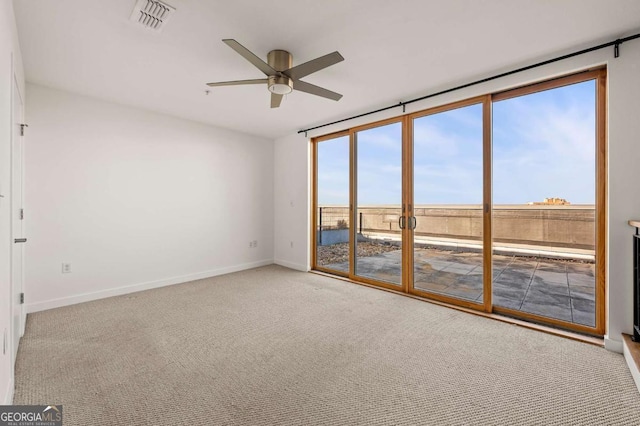 carpeted spare room featuring expansive windows and ceiling fan