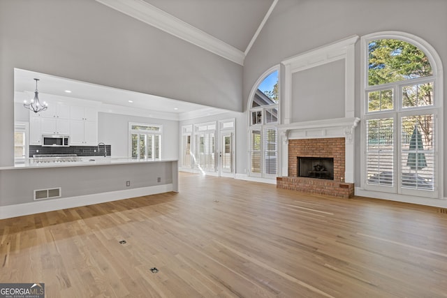 unfurnished living room with high vaulted ceiling, crown molding, a brick fireplace, an inviting chandelier, and light hardwood / wood-style flooring