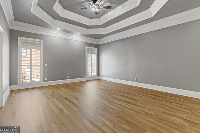 empty room featuring crown molding, ceiling fan, a tray ceiling, and light hardwood / wood-style flooring