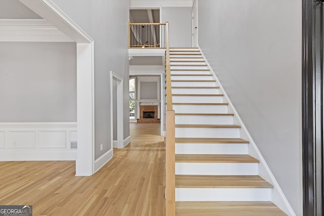 stairs featuring hardwood / wood-style floors, crown molding, a fireplace, and a high ceiling