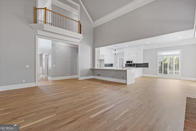 unfurnished living room featuring a notable chandelier, crown molding, light wood-type flooring, and a high ceiling