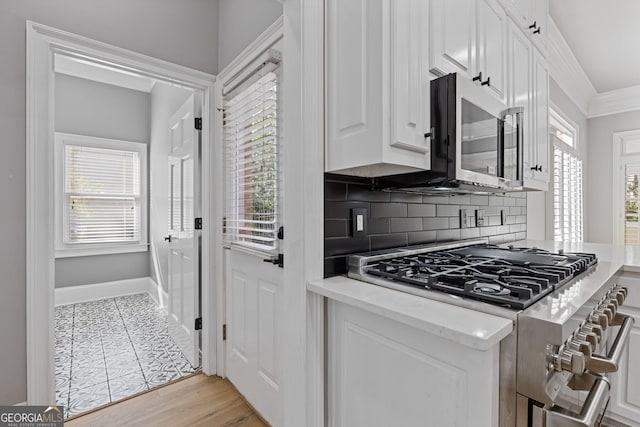 kitchen with appliances with stainless steel finishes, ornamental molding, white cabinets, decorative backsplash, and light wood-type flooring