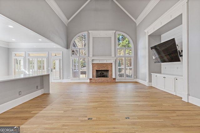 unfurnished living room featuring crown molding, high vaulted ceiling, light wood-type flooring, a healthy amount of sunlight, and a fireplace