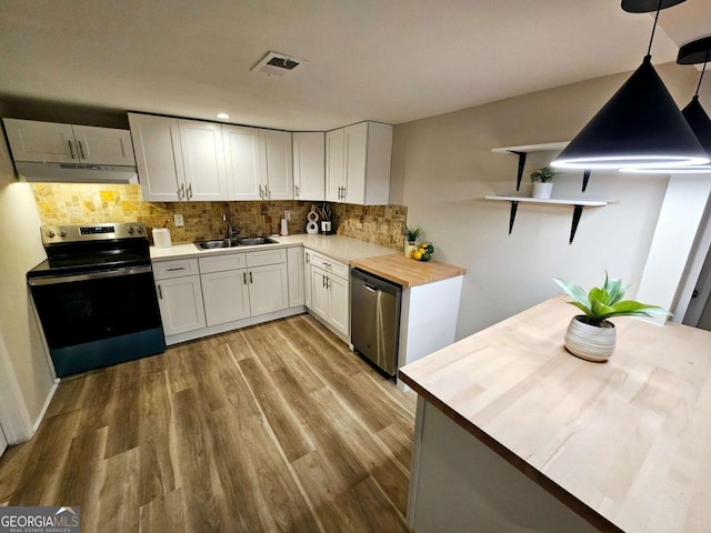 kitchen featuring sink, butcher block counters, white cabinetry, stainless steel appliances, and decorative light fixtures