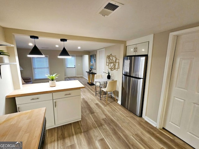 kitchen featuring butcher block countertops, light wood-type flooring, stainless steel fridge, pendant lighting, and white cabinets