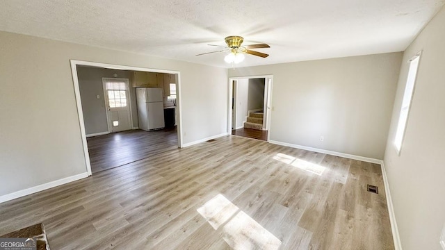 spare room with a ceiling fan, stairs, baseboards, and light wood-type flooring