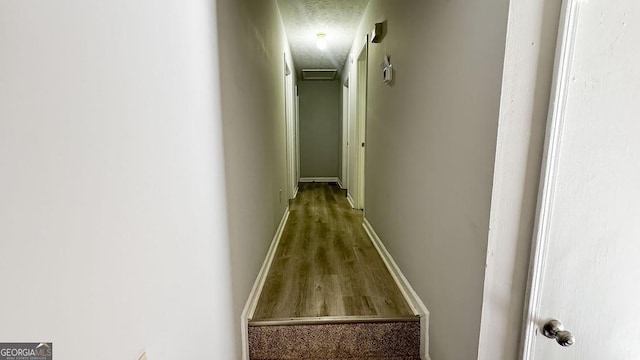 hall with wood finished floors, baseboards, and a textured ceiling
