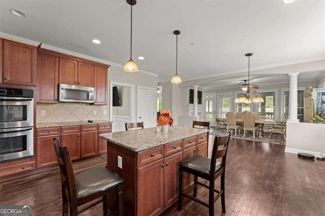 kitchen featuring appliances with stainless steel finishes, a kitchen breakfast bar, decorative light fixtures, and ornate columns