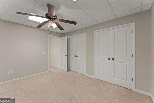 unfurnished bedroom with two closets, a paneled ceiling, light colored carpet, and ceiling fan