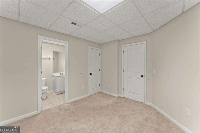 unfurnished bedroom with light colored carpet, connected bathroom, and a paneled ceiling