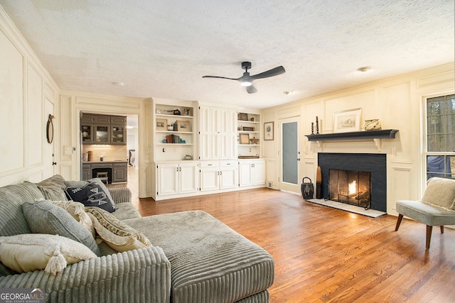 living room with built in shelves, ceiling fan, a textured ceiling, and light wood-type flooring