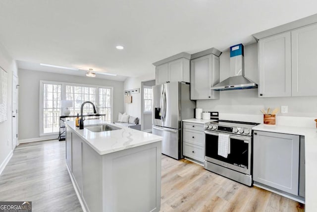 kitchen with wall chimney range hood, sink, gray cabinets, appliances with stainless steel finishes, and light stone countertops