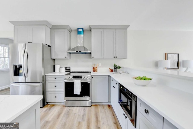 kitchen featuring wall chimney range hood, light hardwood / wood-style floors, and appliances with stainless steel finishes