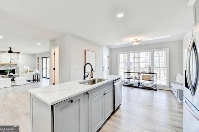 kitchen with a fireplace, sink, stainless steel dishwasher, light stone countertops, and a center island with sink