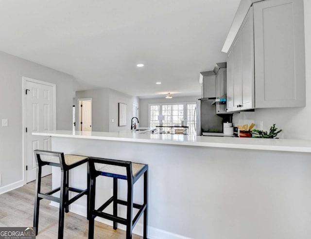 kitchen featuring sink, stainless steel refrigerator, a kitchen bar, kitchen peninsula, and light wood-type flooring