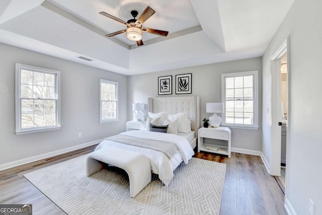 bedroom with a tray ceiling, ceiling fan, and light wood-type flooring