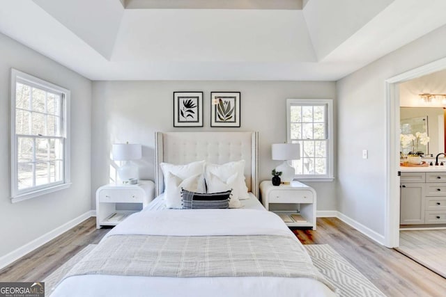 bedroom with sink, a tray ceiling, ensuite bath, and hardwood / wood-style flooring