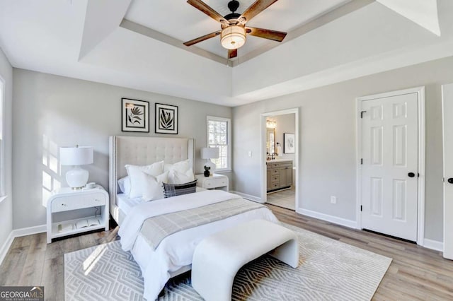 bedroom with connected bathroom, light hardwood / wood-style flooring, a raised ceiling, and ceiling fan