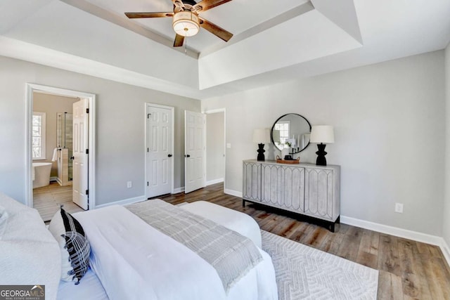 bedroom with connected bathroom, hardwood / wood-style floors, a raised ceiling, and ceiling fan