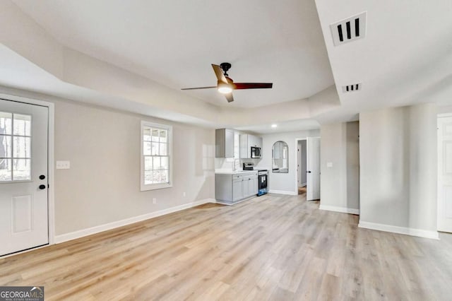 unfurnished living room featuring light hardwood / wood-style flooring, ceiling fan, and a tray ceiling