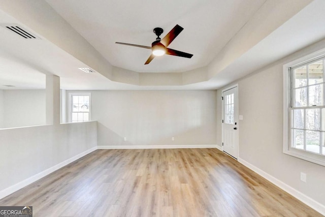 empty room with a tray ceiling, light hardwood / wood-style floors, and ceiling fan