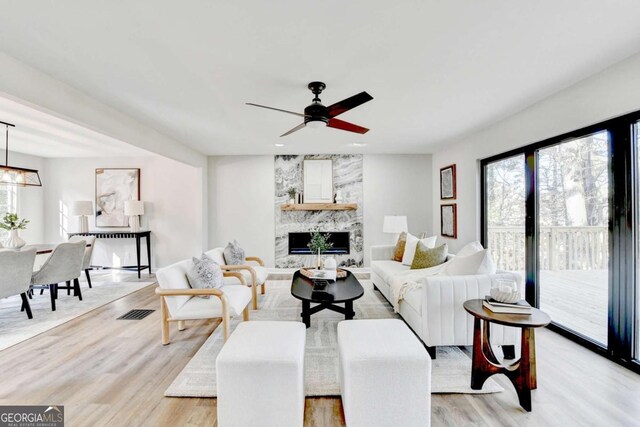 living room with a large fireplace, ceiling fan with notable chandelier, and light hardwood / wood-style floors