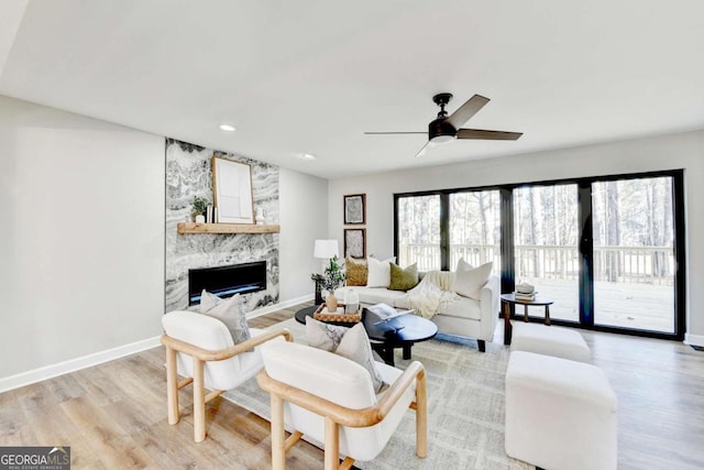 living room with ceiling fan, a large fireplace, and light hardwood / wood-style floors