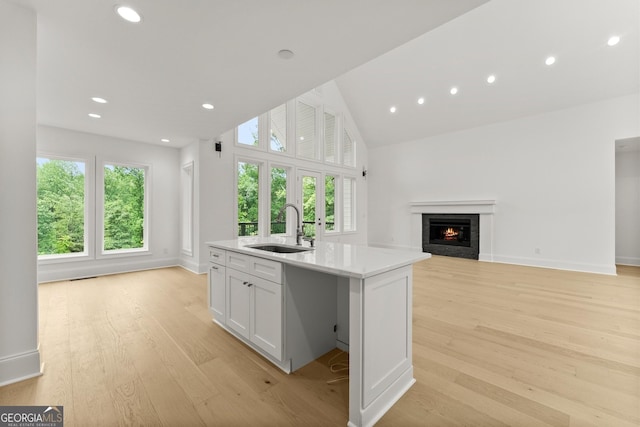 kitchen featuring an island with sink, sink, white cabinets, and light hardwood / wood-style flooring