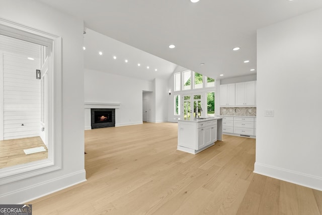 unfurnished living room with lofted ceiling, sink, and light hardwood / wood-style flooring