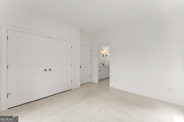 unfurnished bedroom with light colored carpet, ensuite bath, and a closet