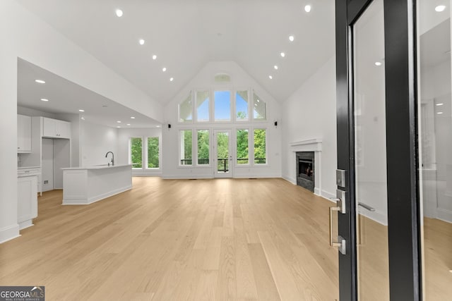 unfurnished living room with high vaulted ceiling, a fireplace, and light hardwood / wood-style flooring