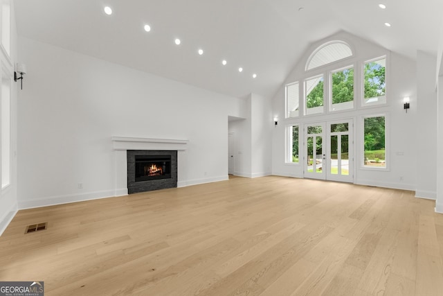 unfurnished living room featuring a tiled fireplace, high vaulted ceiling, and light wood-type flooring