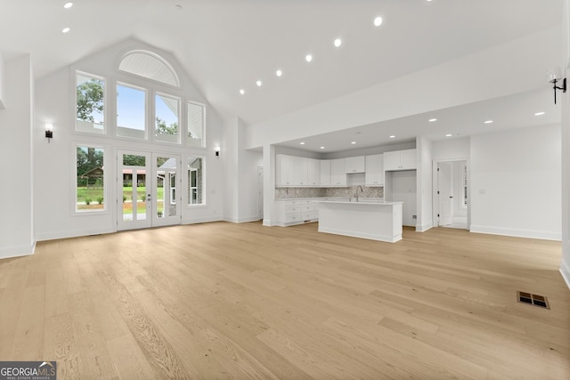 unfurnished living room featuring french doors, high vaulted ceiling, sink, and light hardwood / wood-style floors