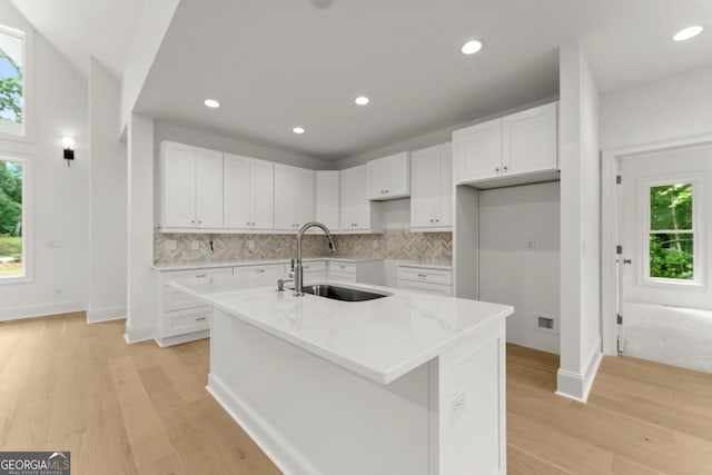 kitchen featuring sink, white cabinets, decorative backsplash, light stone countertops, and a center island with sink