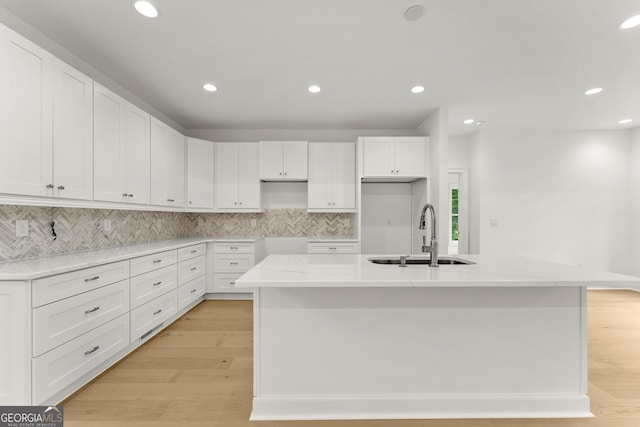 kitchen with white cabinets, sink, a kitchen island with sink, and light hardwood / wood-style flooring