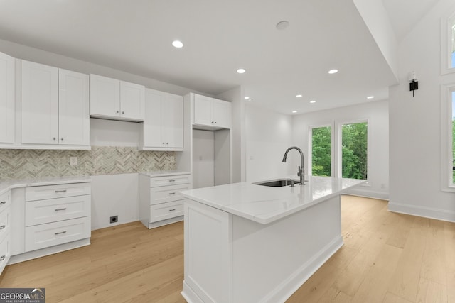 kitchen featuring an island with sink, sink, white cabinets, and light stone counters