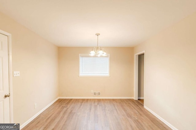 empty room featuring a notable chandelier and light hardwood / wood-style flooring