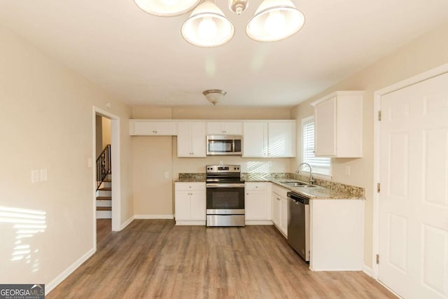 kitchen with appliances with stainless steel finishes, white cabinetry, sink, light stone counters, and light hardwood / wood-style flooring