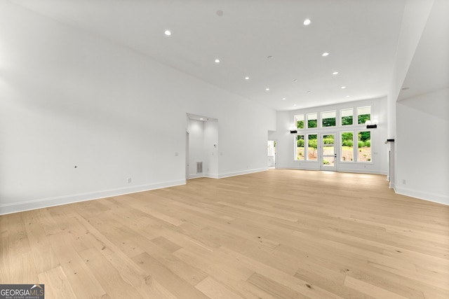 unfurnished living room with a towering ceiling and light wood-type flooring