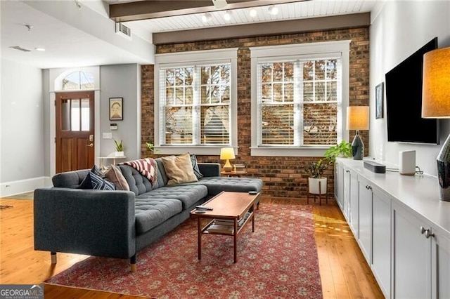 living room with beamed ceiling, brick wall, and light wood-type flooring